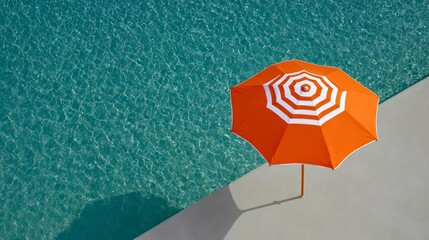 Large orange umbrella is sitting on a concrete ledge next to a pool. The umbrella is open and the water is calm. Scene is peaceful and relaxing