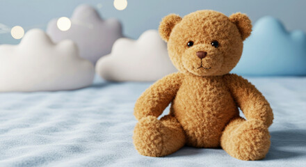 Cute brown teddy bear sitting on soft blue blanket with cloud shape pillows and string lights in background. Child toy for baby room decoration or nursery decor.
