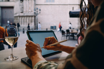 Focused woman draws digitally on tablet while sitting in street cafe, portraying concentration, digital technique and freedom of freelance work in urban outdoor setting.