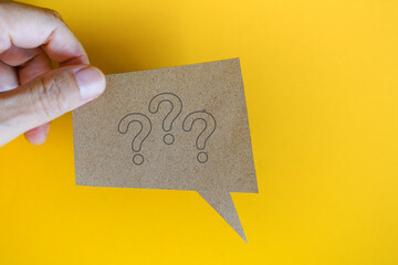 For FAQ , Frequently asked questions concept, asked questions  and answers. Hand hold real brown speech bubble paper cut with question mark on yellow background