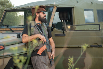 Airsoft sniper in camouflage gear next to vehicle