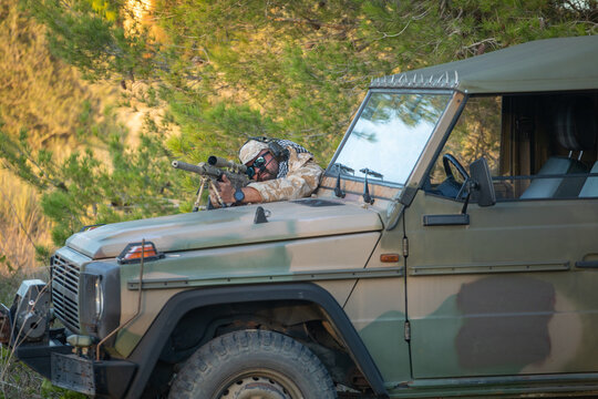 Sniper in camouflage aiming from military vehicle