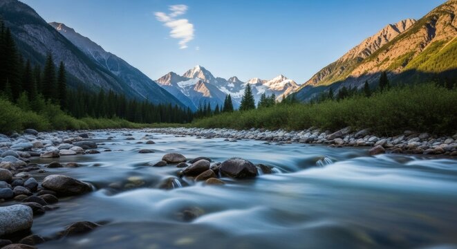 A scenic mountain river flows through a lush green valley towards snow-capped peaks under a clear blue sky.