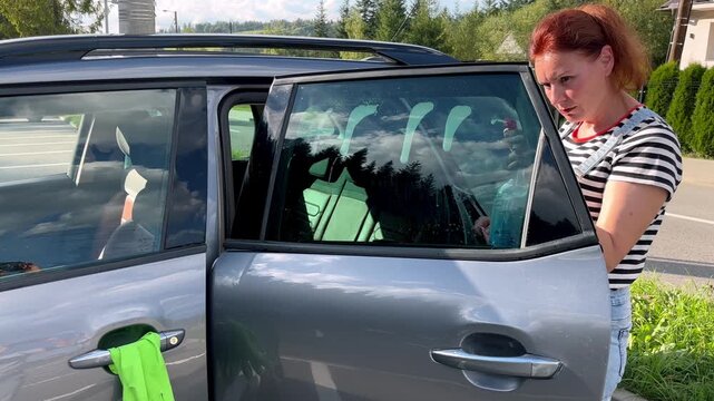 Woman cleaning car window on a parking in sunny day