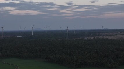 Scenic aerial footage showing wind turbines on hills, a lake with rocky terrain, and a vast mountain range under moody twilight clouds. Drone Footage of Wind Turbines Overlooking a Lake and Mountains - Powered by Adobe
