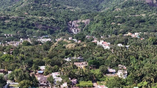 Beautiful aerial footage of Courtallam town with cascading waterfalls, colorful houses, and temples set amid lush greenery and mountain backdrops.