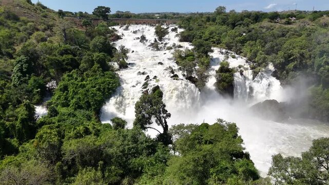Sweeping aerial panorama of Binga Falls, Angola, showing multiple cascading levels surrounded by vivid green jungle and mist rising under bright tropical light