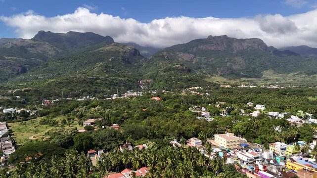 A mesmerising aerial view of a lush South Indian town, Courtallam, nestled at the foothills of the Western Ghats, surrounded by dense greenery and towering mist-clad mountains.