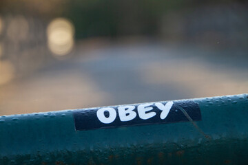 Obey sticker outdoors on wet green pipe with dew or rain