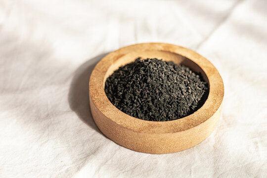Black cumin seeds in a wooden bowl on a white cloth