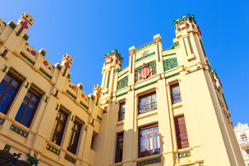 Art Nouveau facade of the Estacio del Nord railway station in Valencia, Spain. Intricate design with colored stonework adorned mosaic tiles depicting Valencian motifs like oranges and stars under sky