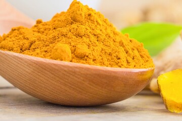 Vibrant turmeric powder in a wooden spoon with roots and leaves