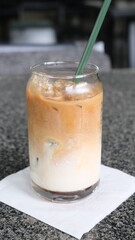 Layered iced latte served in a clear glass with a green straw, placed on a napkin over a granite countertop surface.