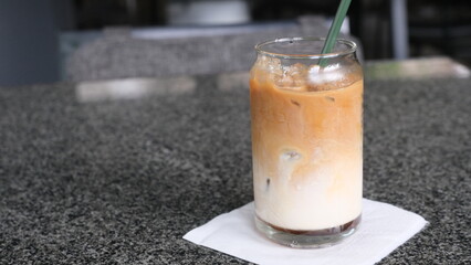 Layered iced latte served in a clear glass with a green straw, placed on a napkin over a granite countertop surface.