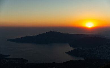 Tranquil sunset slides below dark distant mountains, casting warm orange light