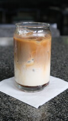 A refreshing iced latte with milk and espresso served in a clear glass jar, placed on a napkin over a granite table surface.