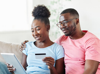 portrait of happy smiling young couple using a tablet computer and a credit card for online shopping at home, technology and internet use in everyday life concept