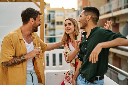 Happy young people having fun during a rooftop party during a summer holiday, standing on the rooftop terrace talking, eating and drinking, love, romance, relationship, flirting and youth culture conc