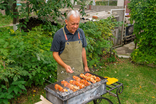 Man grilling in garden wearing apron while cooking skewer - Powered by Adobe