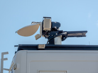 Close-up of a roof‑mounted parabolic satellite dish and electronics on a vehicle used for mobile broadcasting and communications.