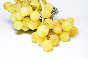 Bunch of yellow grapes in a grey basket on a white background.	Close up.