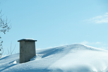 Snow-covered hill with a chimney emerging from the white landscape under a clear blue sky, creating a serene winter atmosphere and inviting tranquility