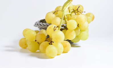 Bunch of yellow grapes in a grey basket on a white background.	