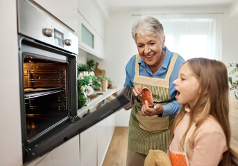 Portrait of grandmother and grandaughter having fun together preparing and eating baked dessert food in kitchen at home, waiting for cookies to be baked  and watching thrgough glass in oven
