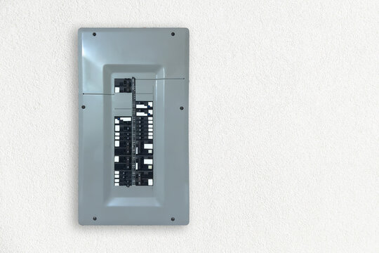 Gray circuit breaker panel with dual columns of breakers mounted on a white textured interior wall, showing electrical distribution hardware.