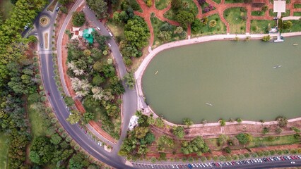 Aerial view of a tranquil lake reflecting the sky, bordered by lush green trees and winding roads, creating a serene contrast of nature and infrastructure, Mendoza, Mendoza Province, Argentina.