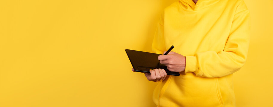 Person in yellow hoodie using digital pen tablet against vibrant yellow background, great for creative, tech, and design themes.