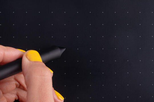 Close-up of a hand holding a stylus on a black graphics tablet with grid dots, ideal for creative design and digital illustration concepts.