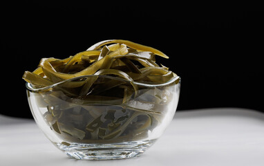 Seaweed salad in a transparent glass bowl on a white surface. Healthy food.
