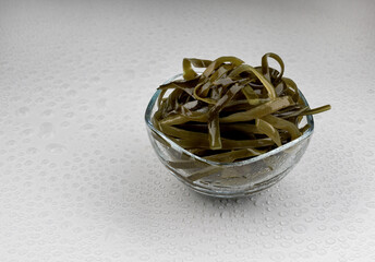 Seaweed salad in a transparent glass bowl on a white surface. Healthy food.