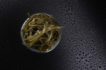 Seaweed salad in a glass cup on a beautiful black background with water drops. Healthy food.