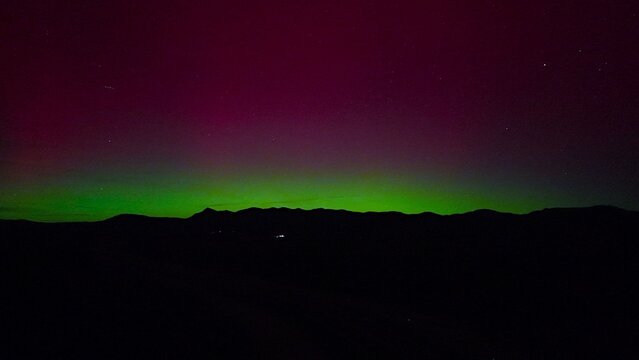 Aerial view of a vibrant aurora borealis paints the night sky with strokes of green and magenta over the dark silhouette of distant mountains, Fruita, Colorado, United States.