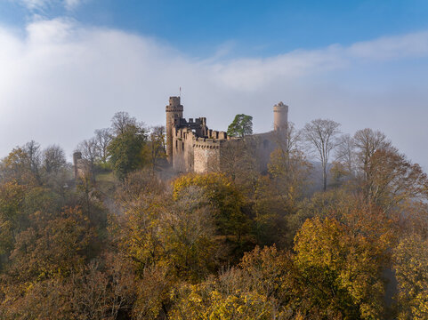 Aerial view of a majestic castle Auerbach perched atop a hill amidst the colorful autumn foliage, partially veiled by a soft, ethereal mist, Bensheim, Hessen, Germany.