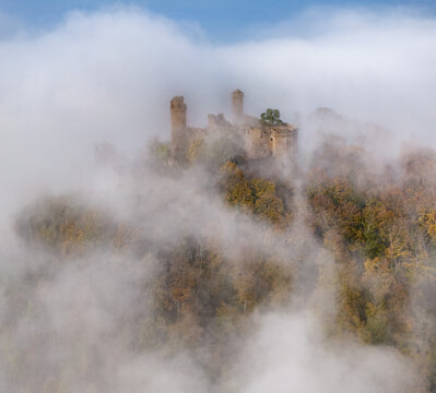Aerial view of Castel Auerbach, an ancient stone structure emerges from a sea of ethereal white fog, contrasting with the warm autumnal hues of the surrounding trees, Bensheim, Hessen, Germany.