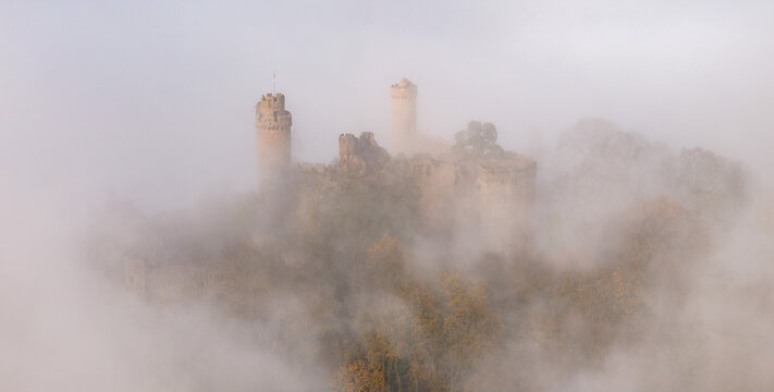 Aerial view of a medieval castle's stone towers piercing through a sea of swirling fog, an ethereal scene of history veiled in mystery, Schloss Auerbach, Bensheim, Hessen, Germany.