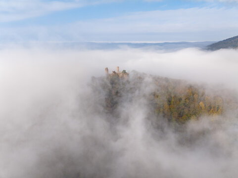 Aerial view of Castle Auerbach emerging from a sea of ethereal fog, a medieval silhouette against the muted autumn landscape, Bensheim, Hessen, Germany.