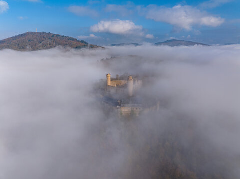Aerial view of medieval castle Auerbach dramatically emerging from a dense sea of fog, its ancient stone walls a beacon of history and mystery, Bensheim, Hessen, Germany.