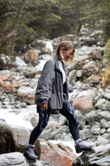 A woman hiking across rocky stones beside a mountain river in Arthurs Pass, New Zealand.