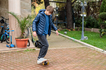 Young teenage boy performing a trick or jump on a skateboard outdoors, showing dynamic action and movement on a brick driveway