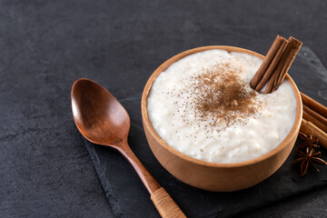Rice pudding with cinnamon in wooden bowl on black background. Copy space