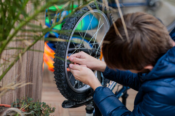 Close-up of a child's hands using a red hand pump to inflate a flat bicycle tire, showing repair and self-reliance outdoors