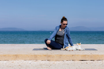 Woman practicing yoga with a cat by the ocean