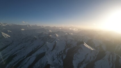 A breathtaking view of a snow-covered mountain range illuminated by bright sunlight, showcasing the rugged terrain and peaks against a clear blue sky, creating a serene and majestic atmosphere