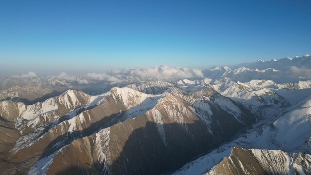 A breathtaking view of a snow-capped mountain range stretches across the horizon, with clear blue skies above and distant peaks partially shrouded in soft clouds, showcasing natural beauty - Powered by Adobe