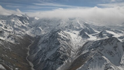 Majestic snow-covered mountain range features dramatic peaks and deep valleys, with clouds hovering above, creating a breathtaking landscape that showcases the beauty of nature's grandeur