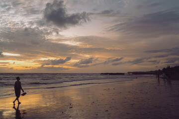Man walking barefoot on the beach at golden sunset holding shoes in hand, expressing solitude, reflection, and peaceful awareness of time and space in motion